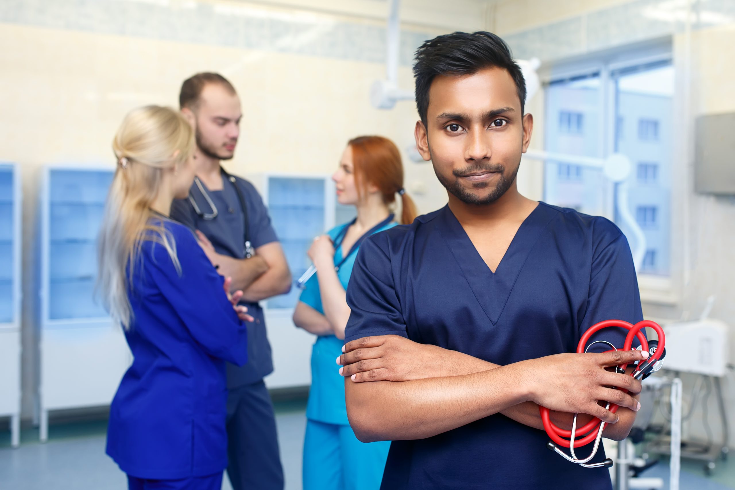 Asian male doctor in front of team, looking at camera with medical team in background